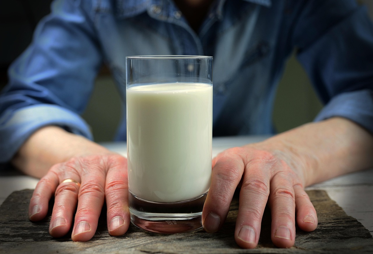 A person wearing a blue shirt has both hands on either side of a glass of milk.